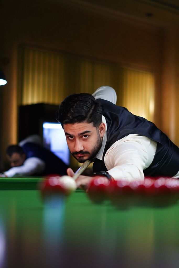 A man in a suit concentrates intensely during a game of pool, poised to strike the cue ball.