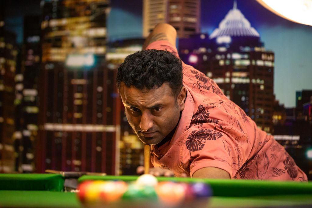 Man aiming in a game of pool with city skyline backdrop indoors, nighttime.