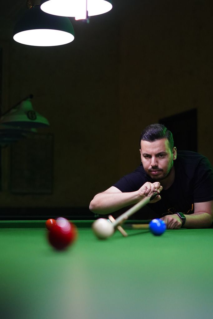 Man concentrating intensely as he lines up a shot in a snooker game indoors.
